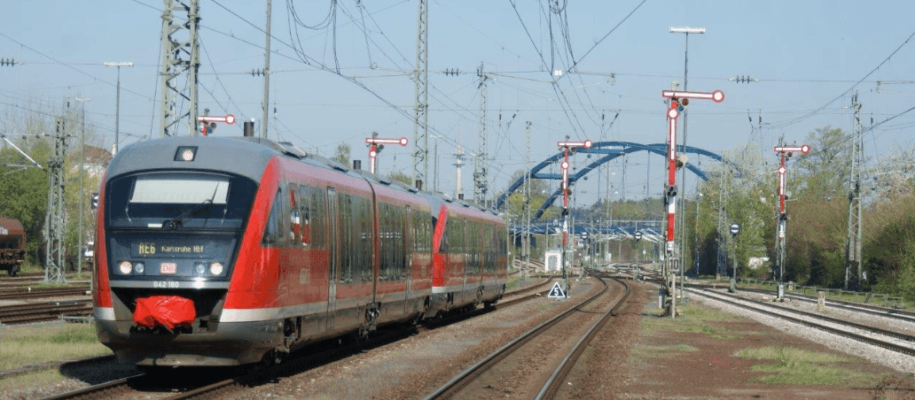 Bahn fährt über Gleise, dahinter eine blaue Brücke